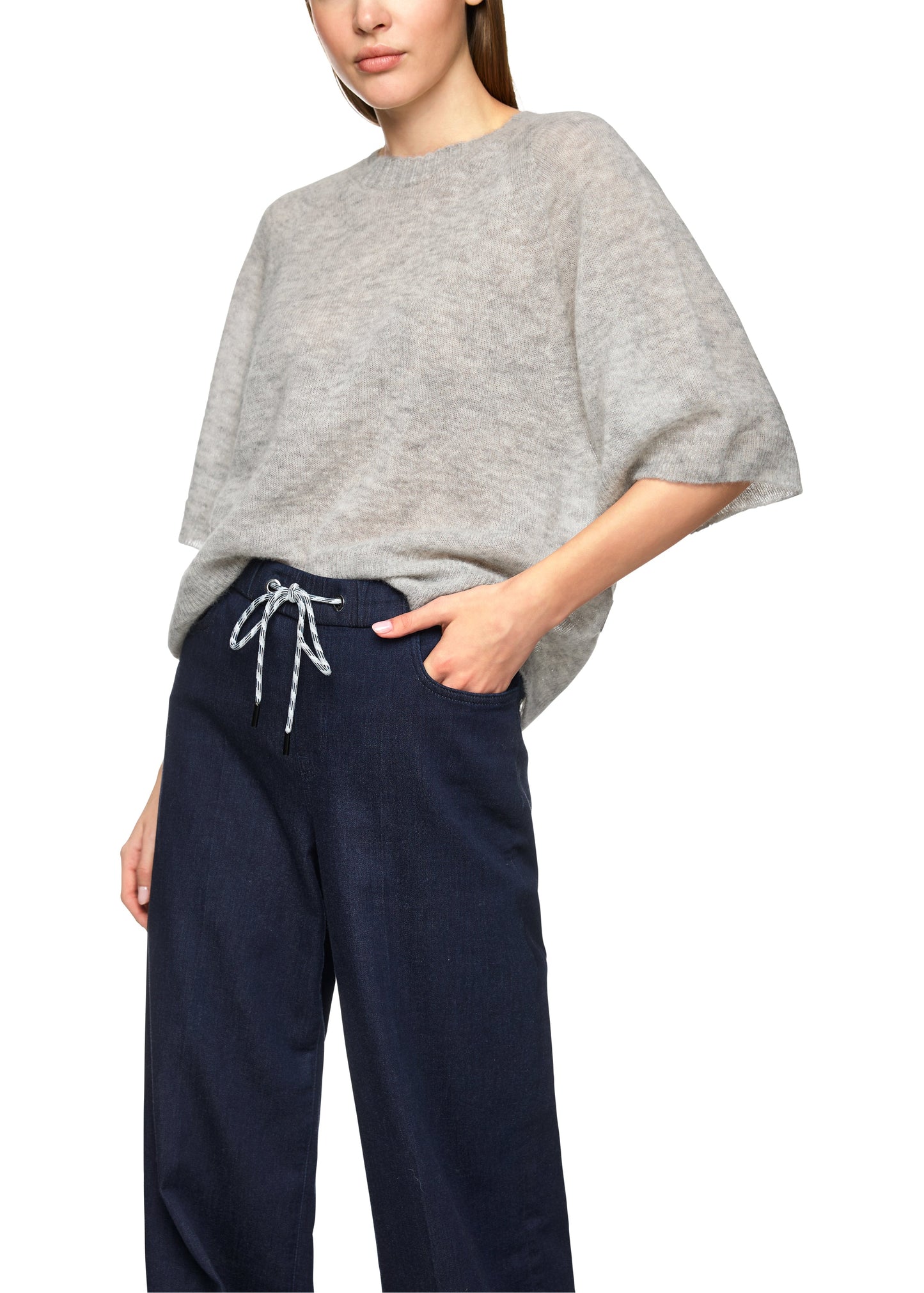 Person wearing a gray oversized sweater and navy pants on a white background