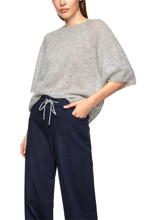 Person wearing a gray oversized sweater and navy pants on a white background