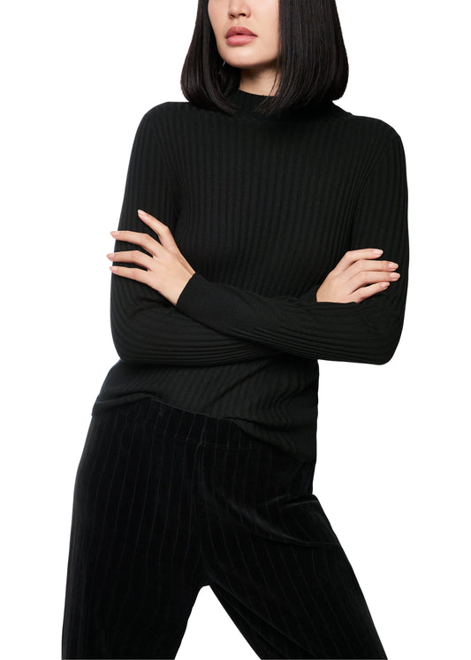 Person wearing a black ribbed turtleneck sweater and black pants on a white background