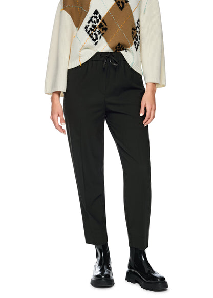 Person wearing a patterned sweater, black pants, and black shoes on a white background