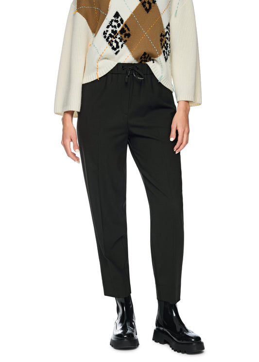 Person wearing a patterned sweater, black pants, and black shoes on a white background