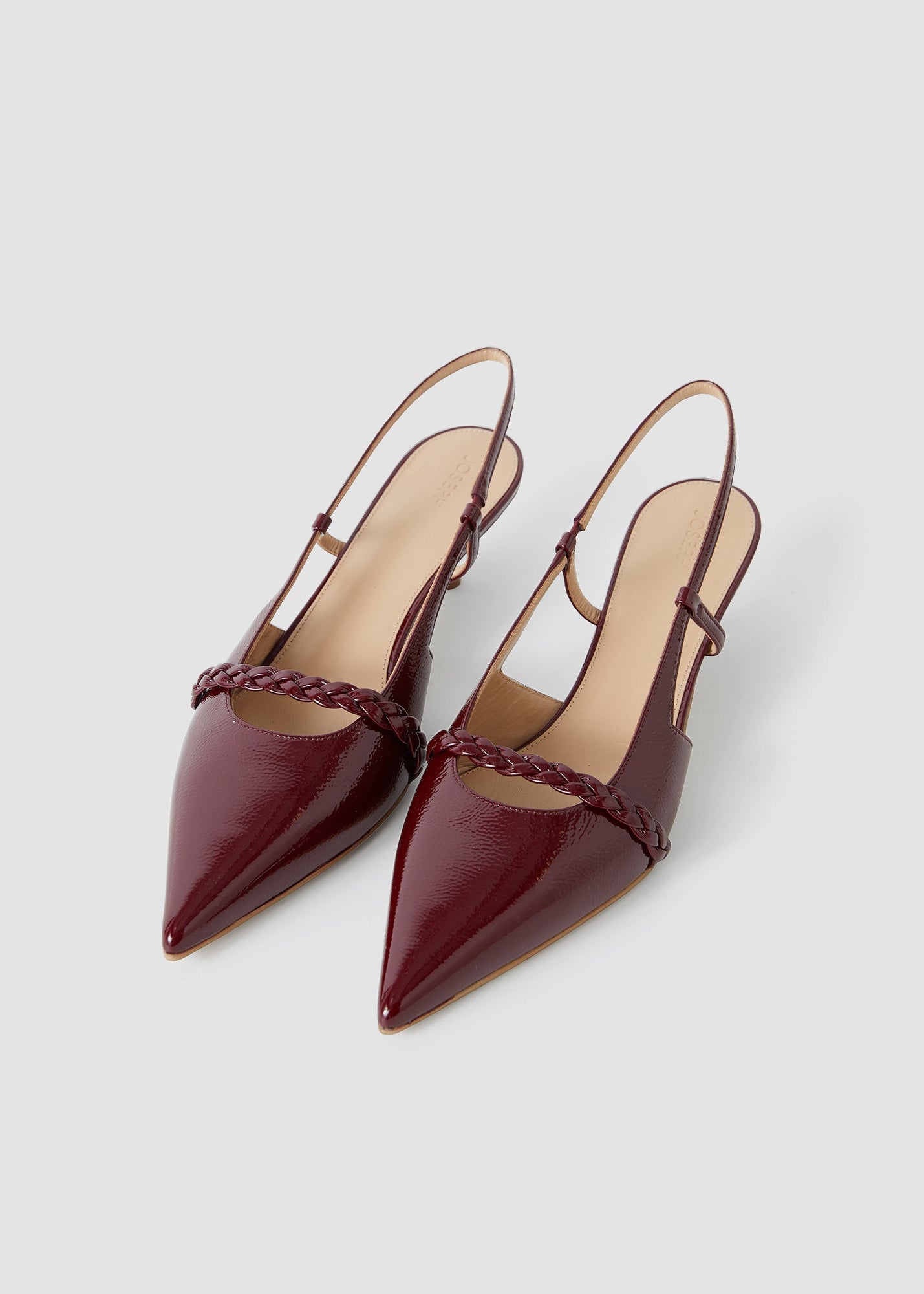 Pair of maroon pointed-toe shoes with thin straps on a light gray background