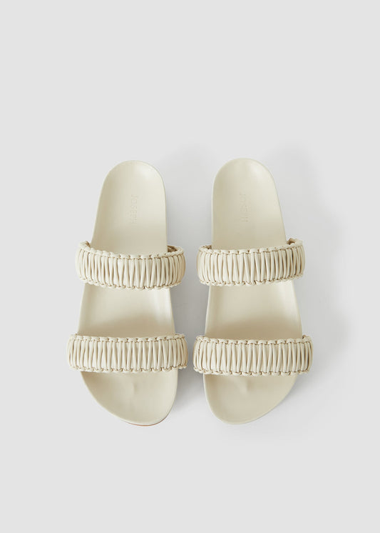 Pair of beige sandals with textured straps on a light gray background