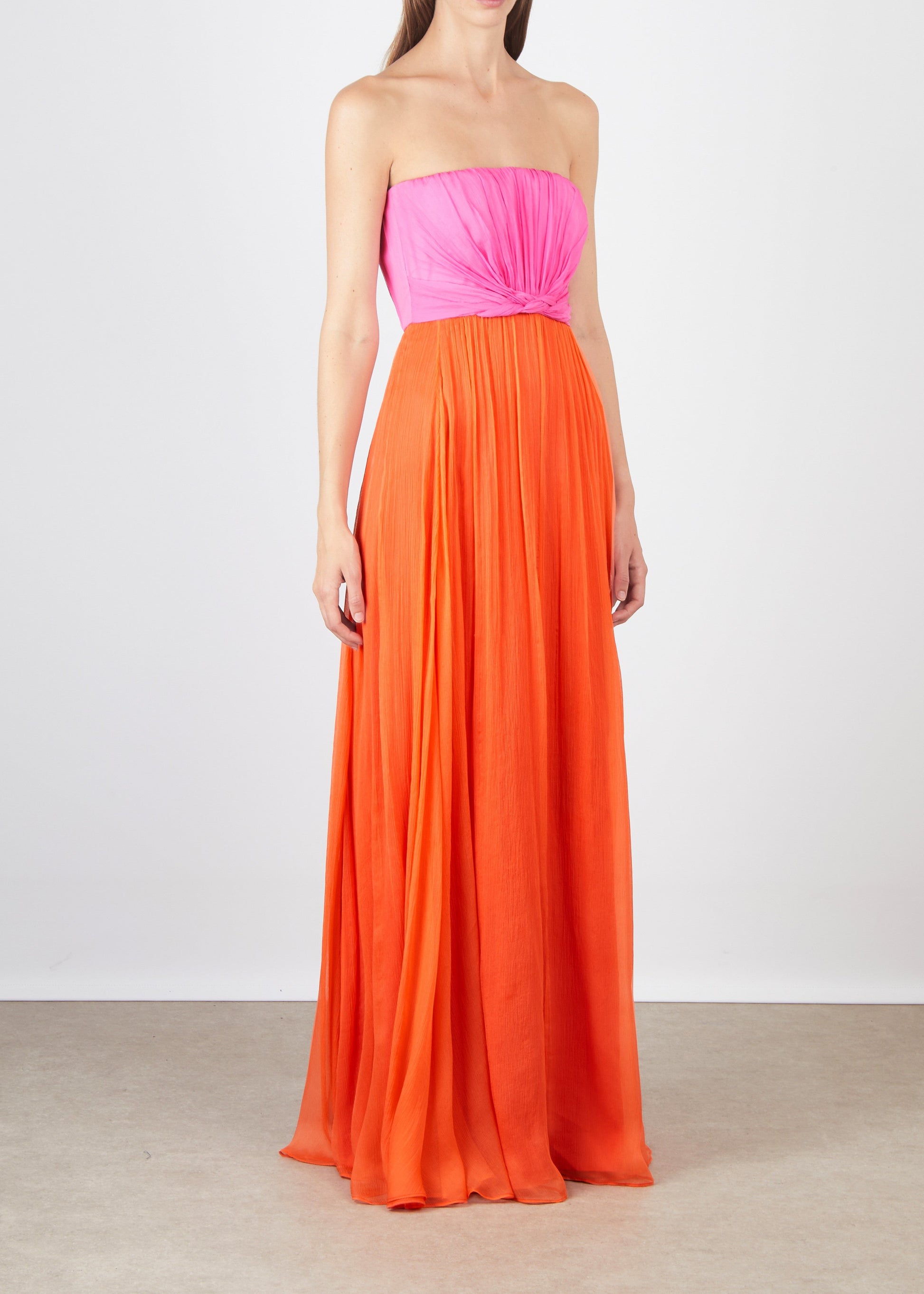 Woman wearing a strapless dress with pink top and orange skirt on a plain background