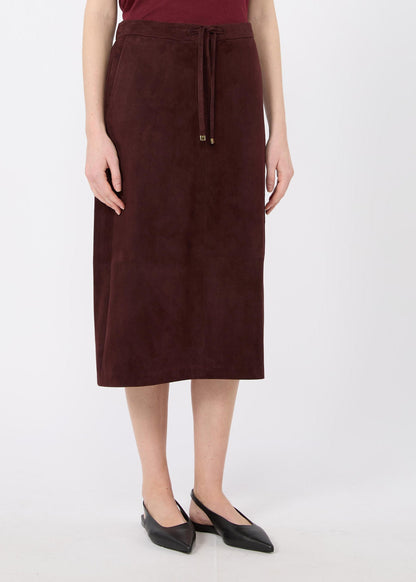 A model wearing a dark brown suede midi skirt with a drawstring waist, paired with black pointed flats, against a plain light gray background.