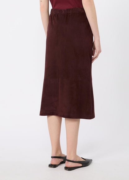 A woman wearing a dark brown midi skirt with an elastic waistband, paired with black flat sandals, shown from the back against a light gray studio background.