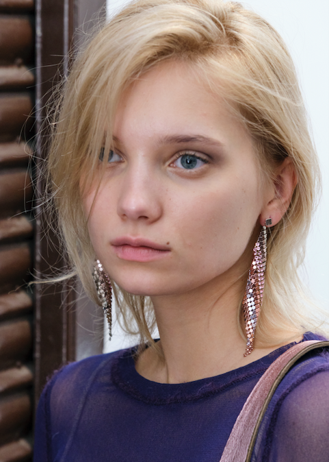 Woman with blonde hair and earrings wearing a purple top.