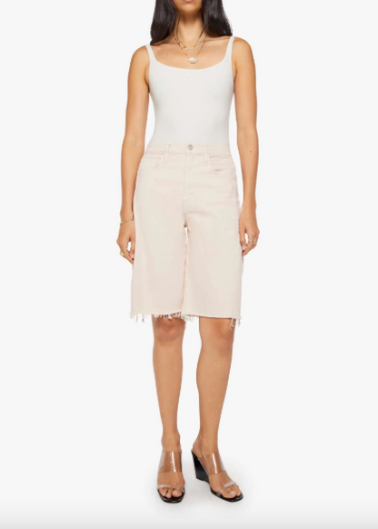 A model wearing a white ribbed tank top and light beige denim shorts with a raw hem, paired with clear-strap heeled sandals, against a plain white background.