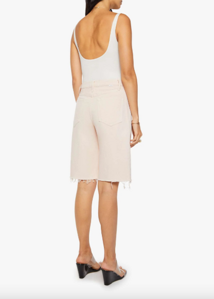 A woman shown from the back wearing a white sleeveless top and light beige denim shorts with a frayed hem, paired with black wedge sandals, against a plain white background.