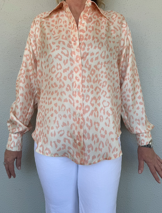 Person wearing a light orange leopard print shirt and white pants against a plain background