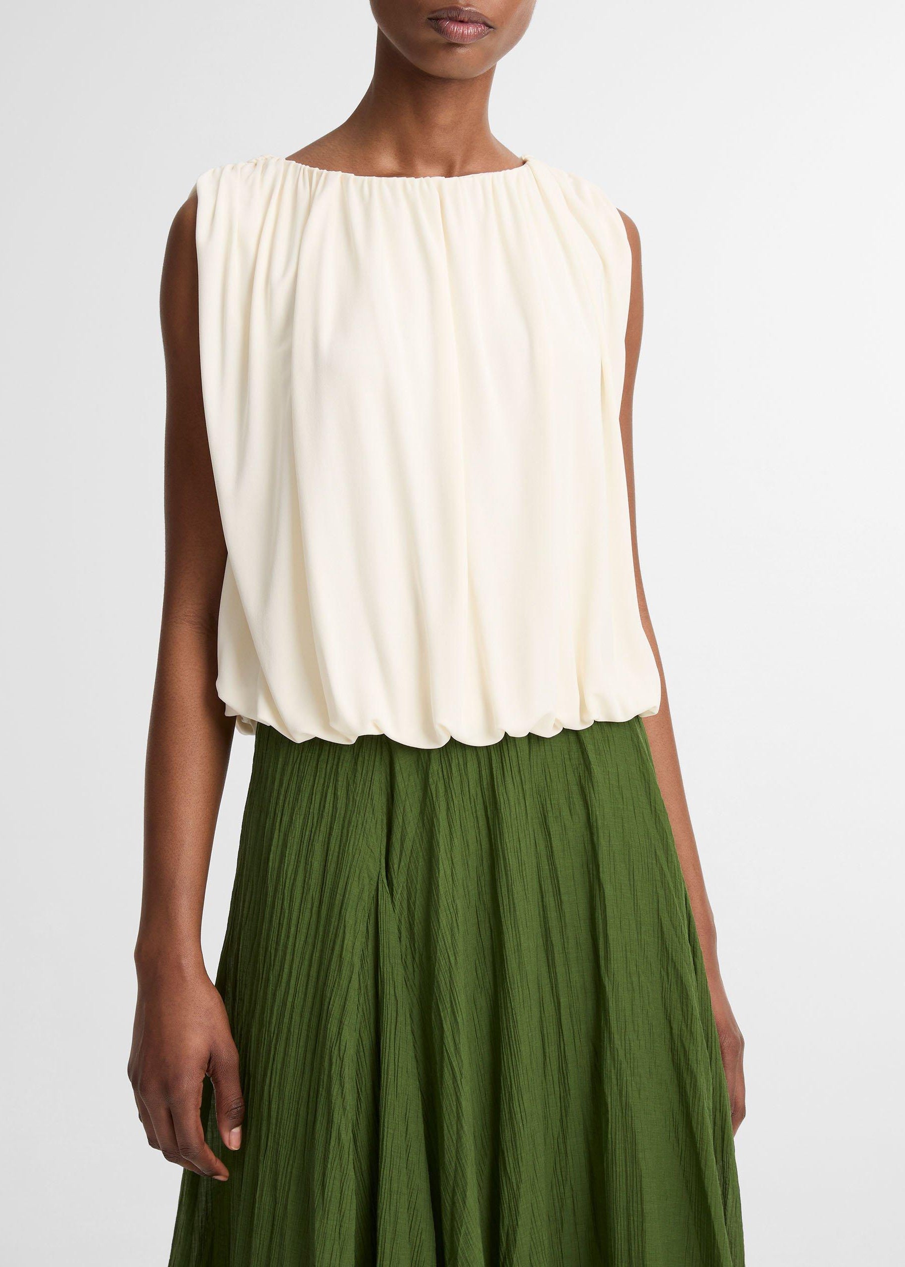 Woman wearing a white sleeveless top and green pleated skirt on a plain background