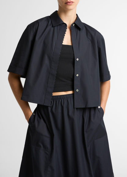 Person wearing a black outfit with a cropped jacket and long pants on a white background