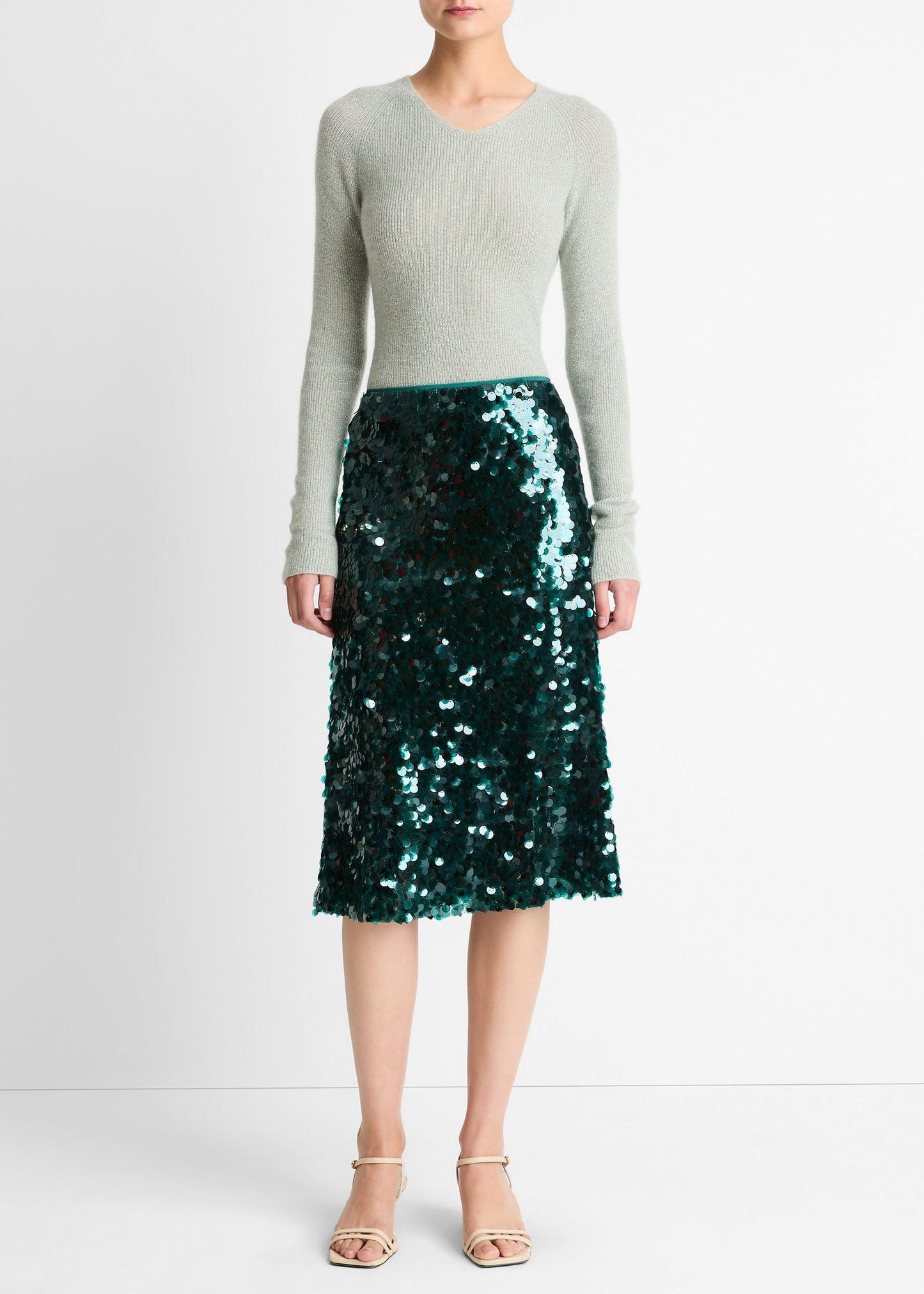 Person wearing a green sequin skirt and light gray sweater on a white background