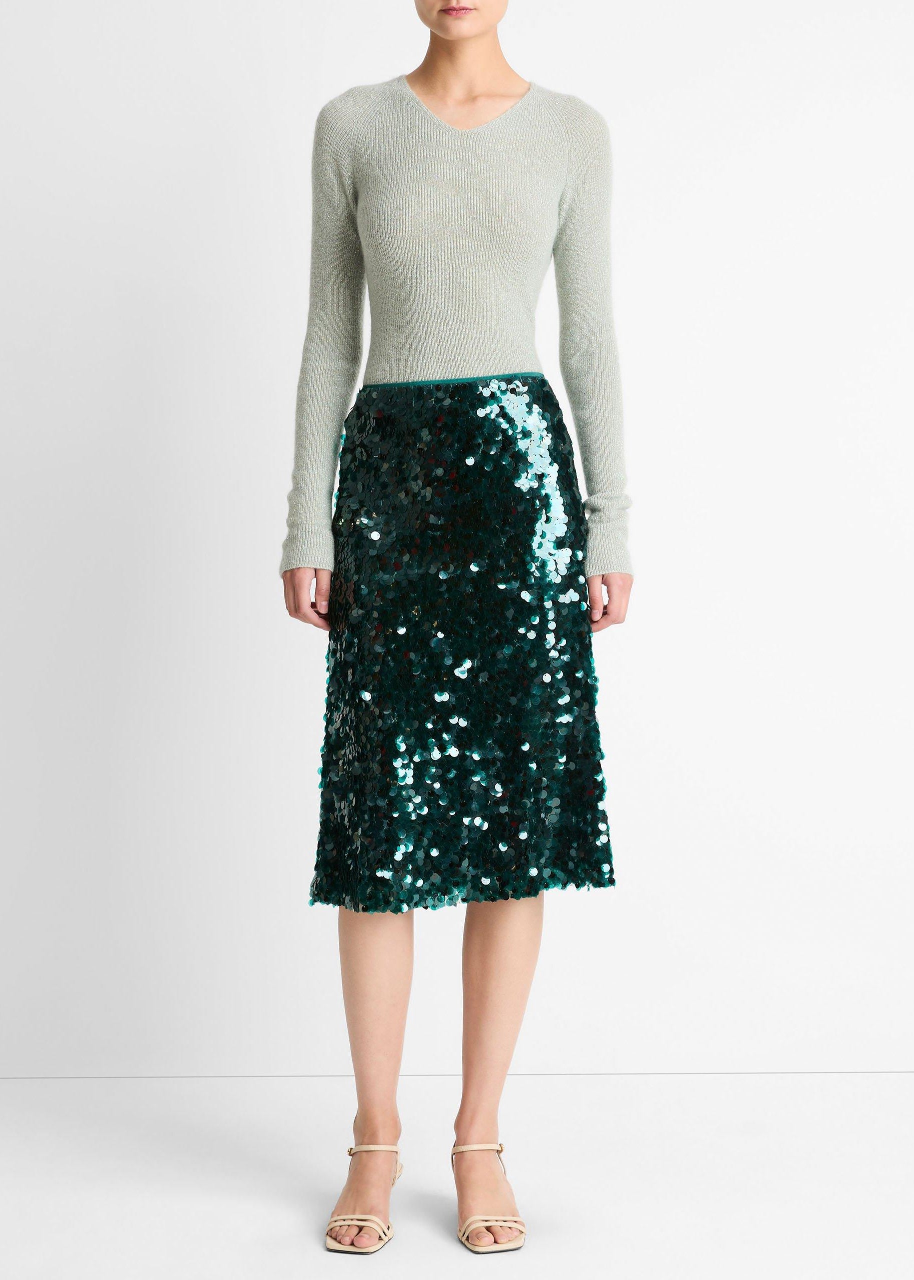 Person wearing a green sequin skirt and light gray sweater on a white background