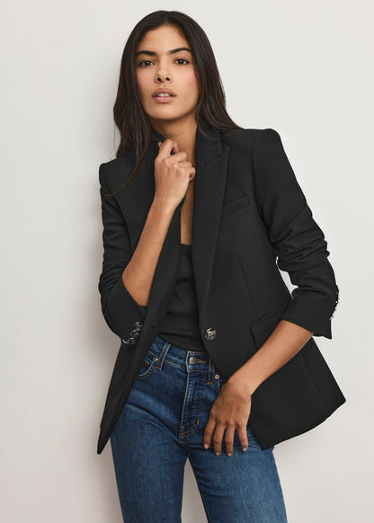 Woman wearing a black blazer and blue jeans against a plain background