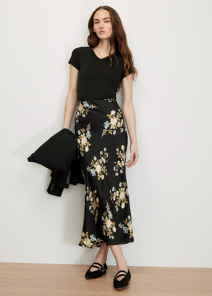 Woman wearing a black top and floral black and white skirt against a white background