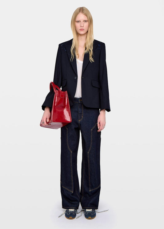 Person wearing a black blazer, blue jeans, and holding a red handbag on a white background