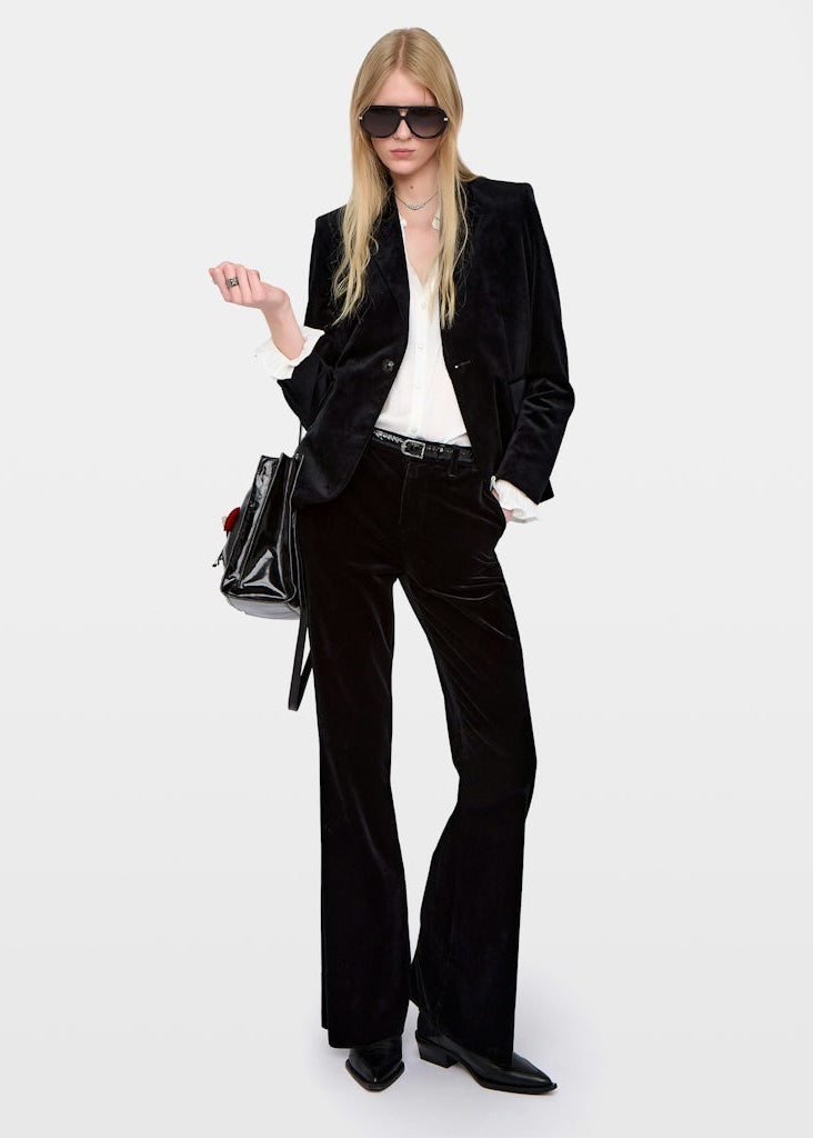 Person wearing a black velvet suit with a white shirt and black shoes on a white background