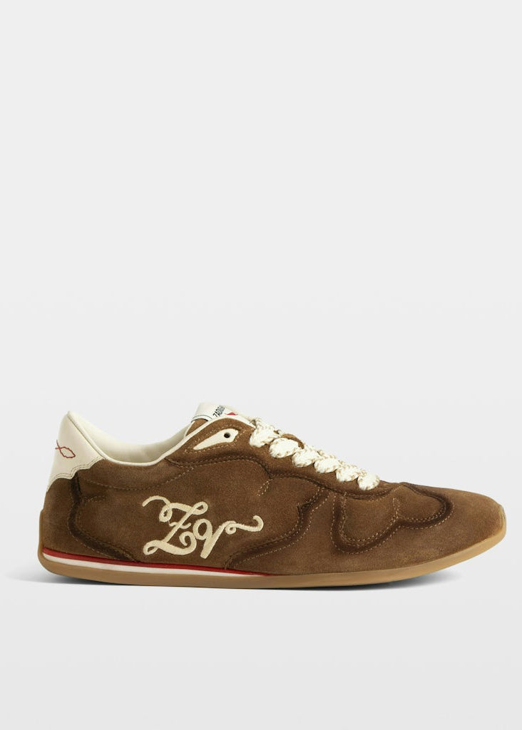 Brown sneaker with white laces and logo on a light gray background