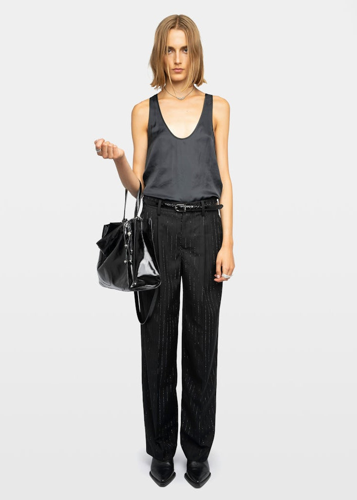 Woman wearing a black sleeveless top and black pants holding a black handbag on a white background