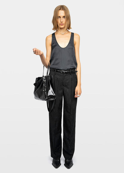 Woman wearing a black sleeveless top and black pants holding a black handbag on a white background