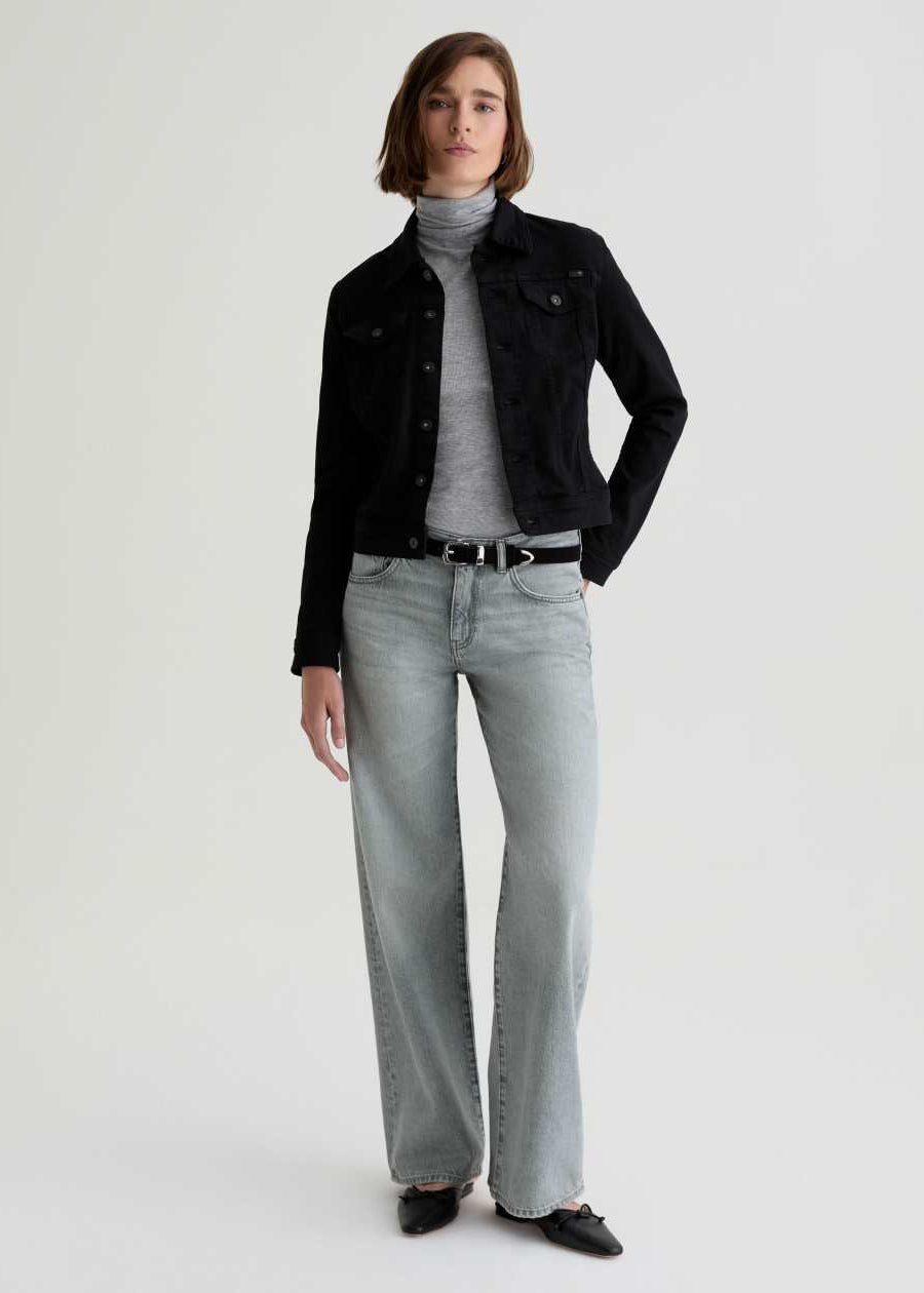 Person wearing a black jacket, gray turtleneck, and light gray jeans on a white background