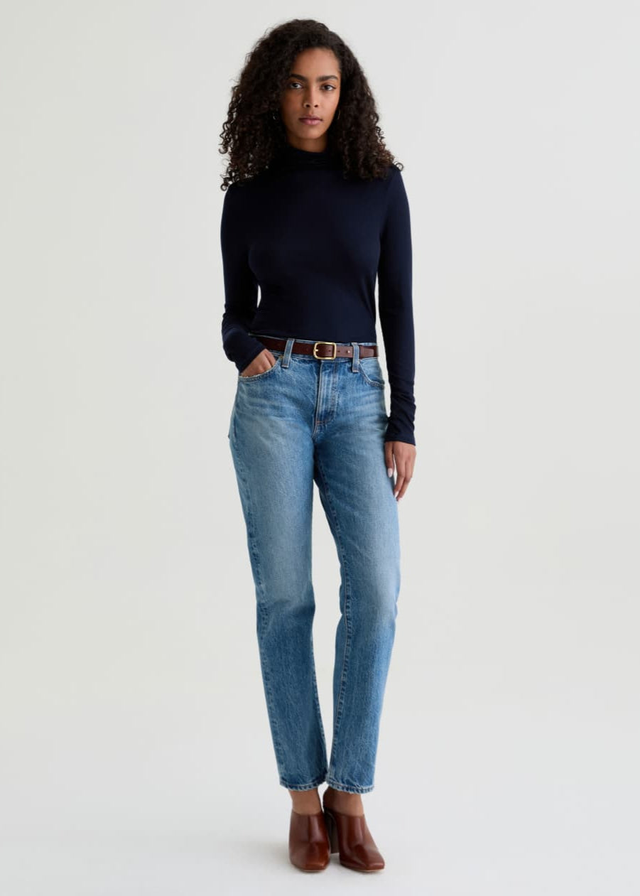 Woman wearing a black long-sleeve top and blue jeans on a white background