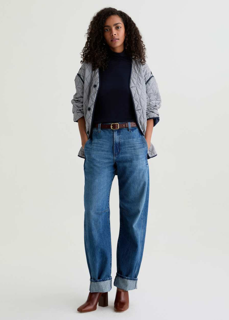 Person wearing a gray cardigan, black top, blue jeans, and brown boots on a white background