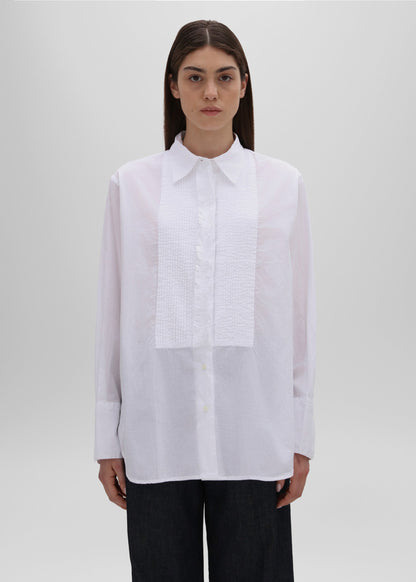 Person wearing a white shirt with a subtle pattern on a plain background