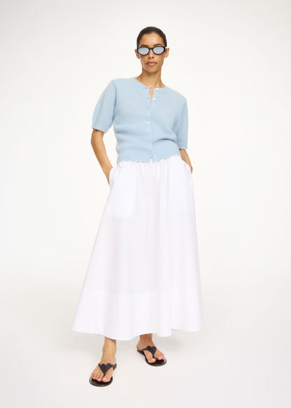 Woman wearing a light blue top and white skirt on a white background