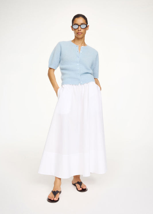 Woman wearing a light blue top and white skirt on a white background