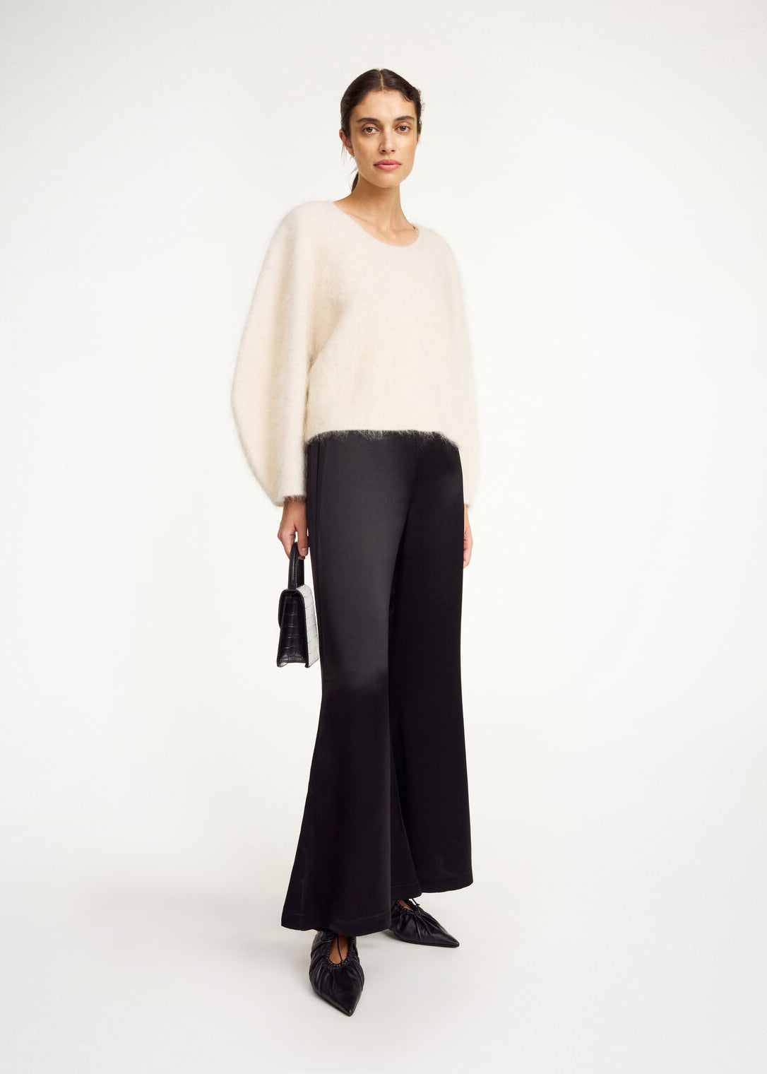 Woman wearing a white sweater and black pants on a white background