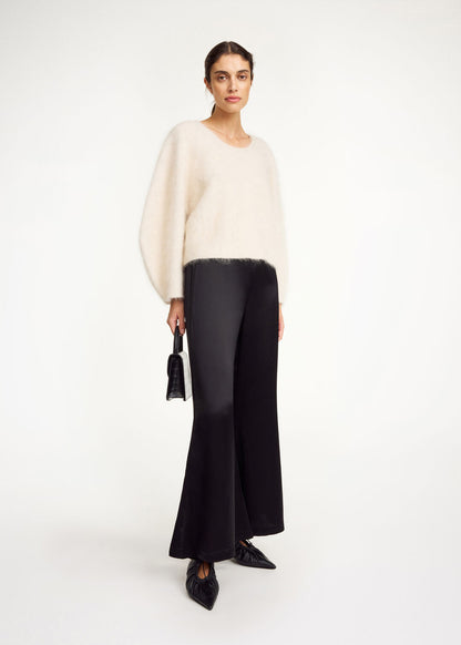 Woman wearing a white sweater and black pants on a white background
