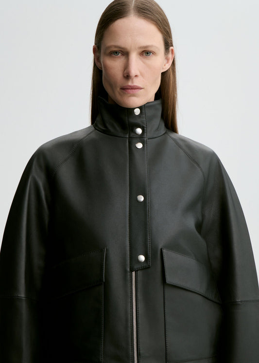 Person wearing a black coat with white buttons on a light gray background