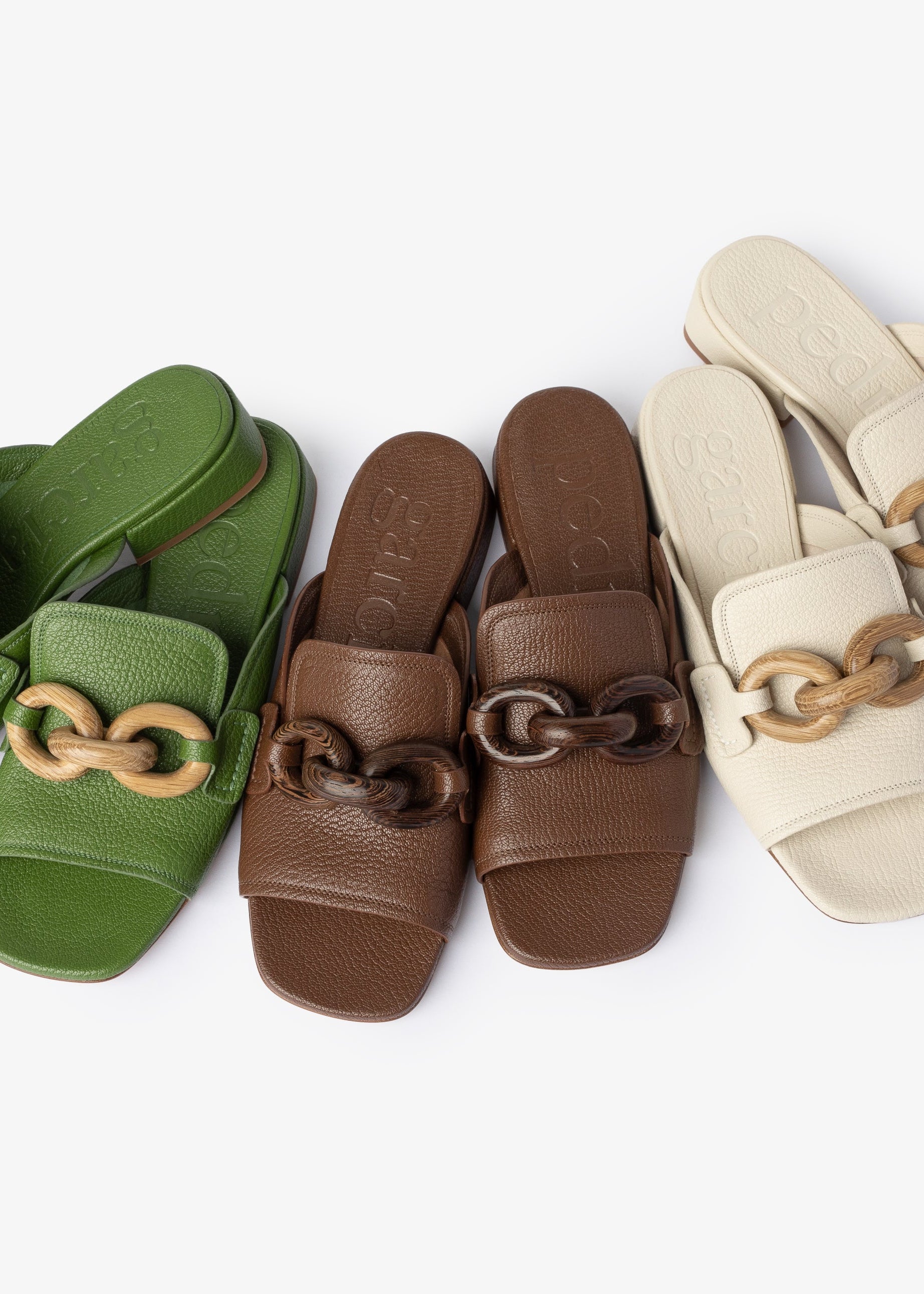 Three pairs of sandals in green, brown, and beige with wooden chain details on a white background.
