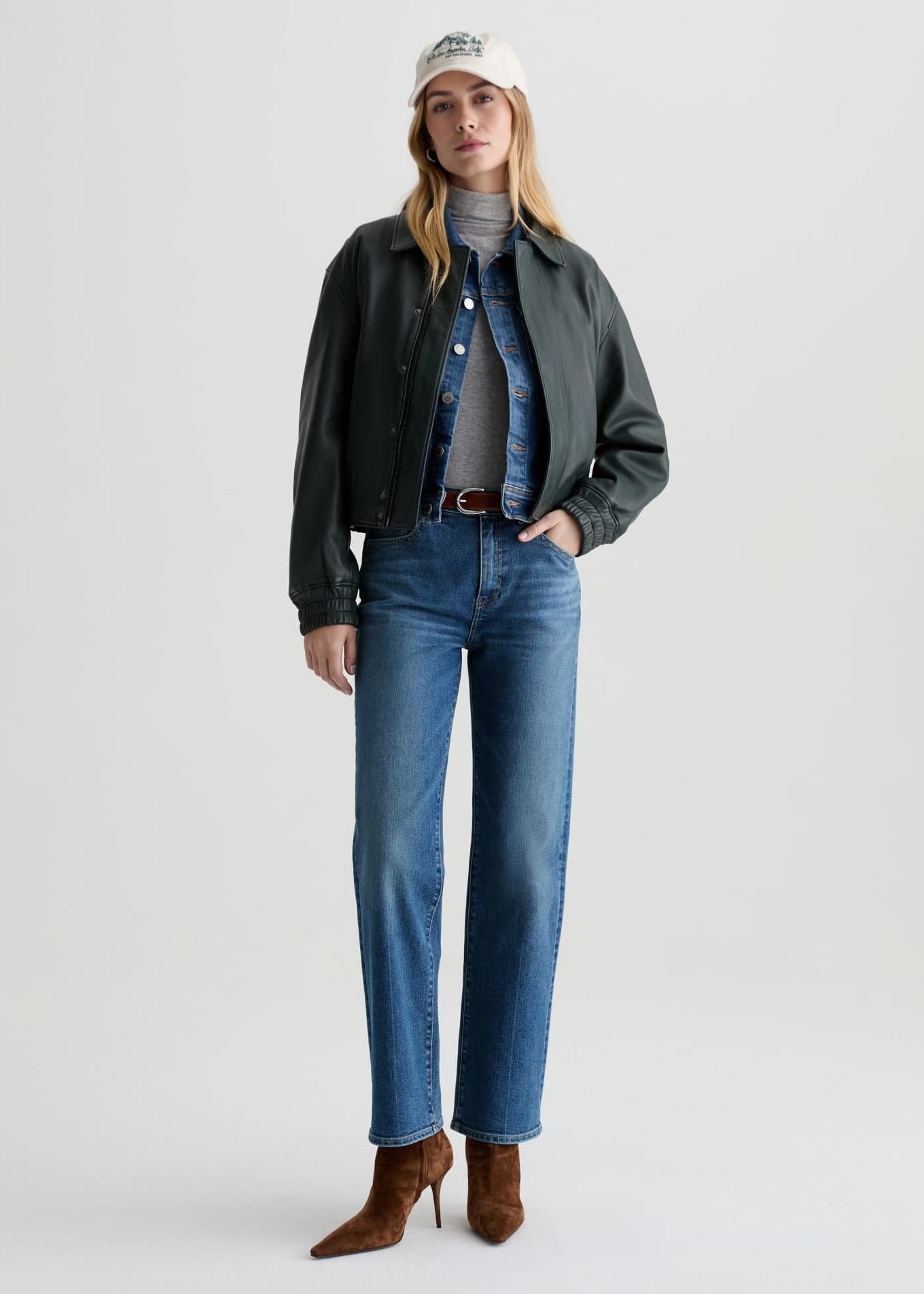 Woman wearing a black jacket, gray turtleneck, blue jeans, and brown boots on a white background
