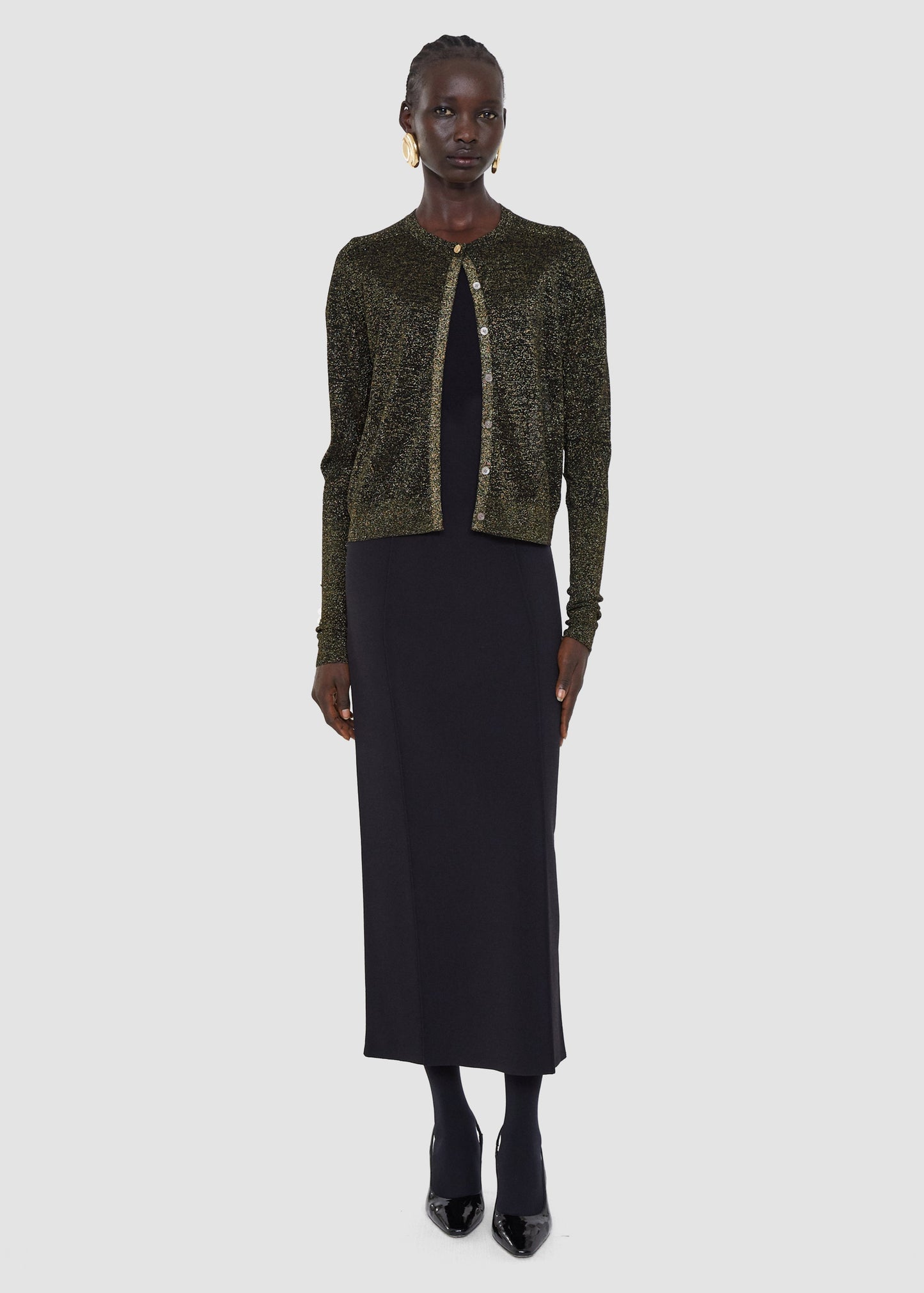Woman wearing a green sequined cardigan over a black dress on a white background