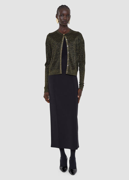 Woman wearing a green sequined cardigan over a black dress on a white background