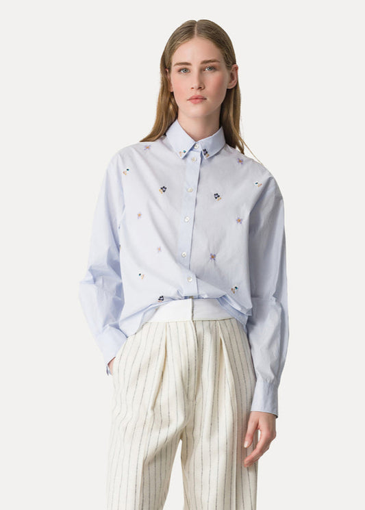 Woman wearing a light blue shirt with floral patterns and white pants on a white background