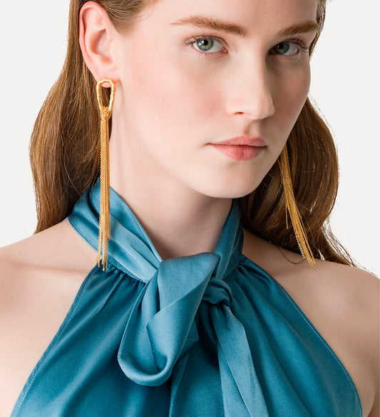 Woman wearing gold earrings with a blue top against a white background