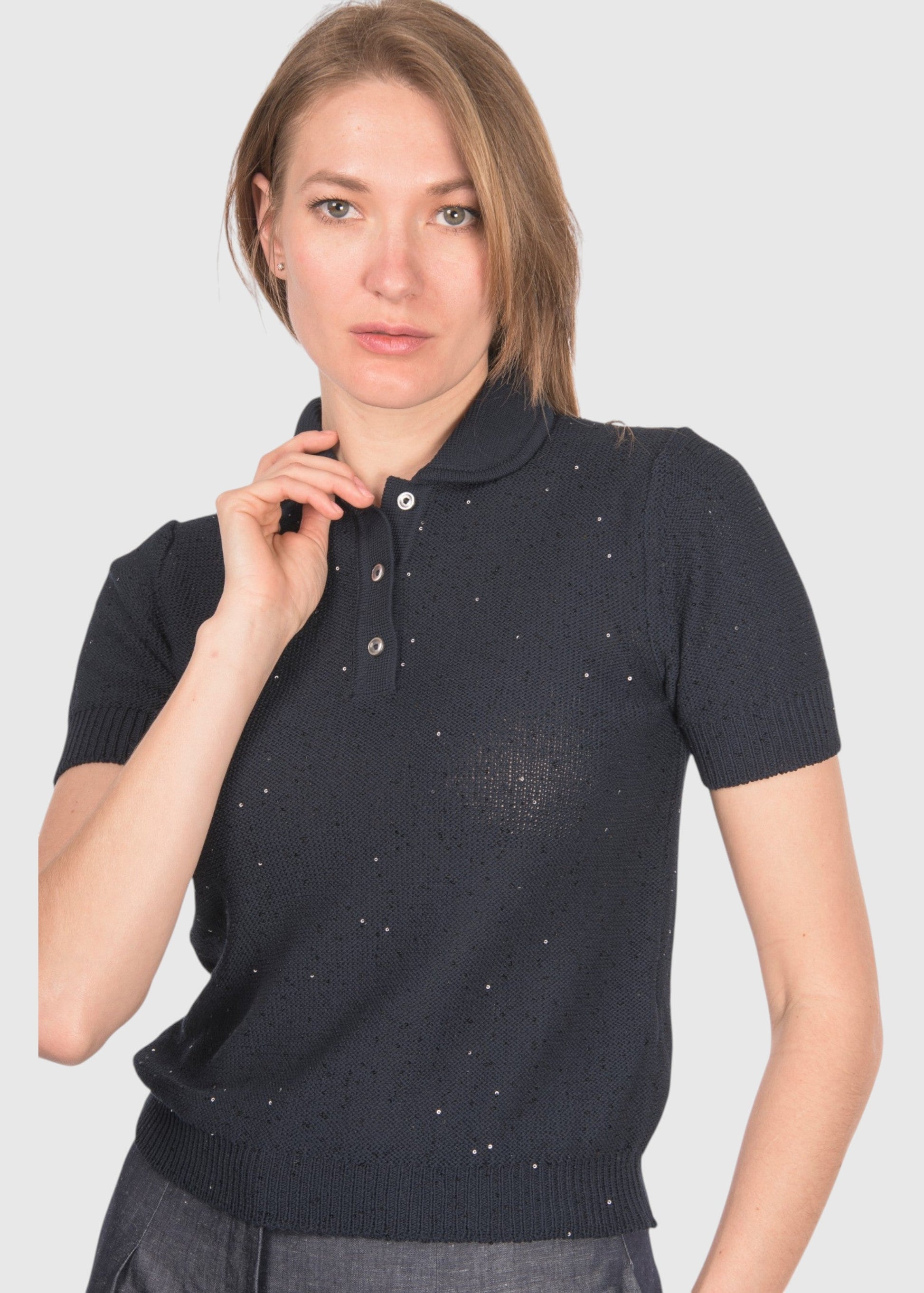 A woman modeling a short-sleeve knit polo shirt in a very dark navy or near-black color with small scattered light reflective dot details, against a plain light gray studio background.