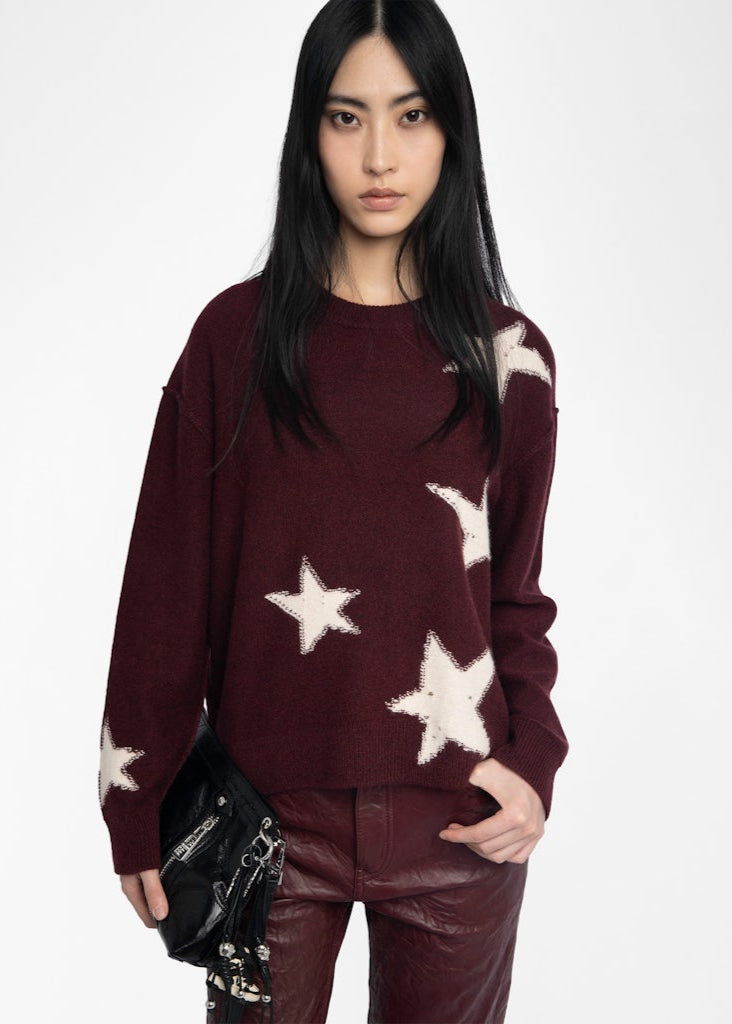 Woman wearing a burgundy sweater with star patterns on a white background
