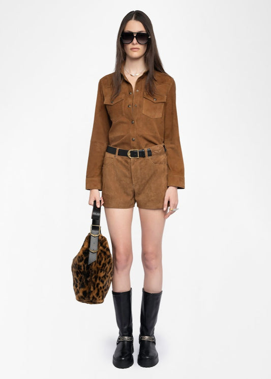 Woman wearing a brown suede outfit with black boots and a leopard print bag on a white background