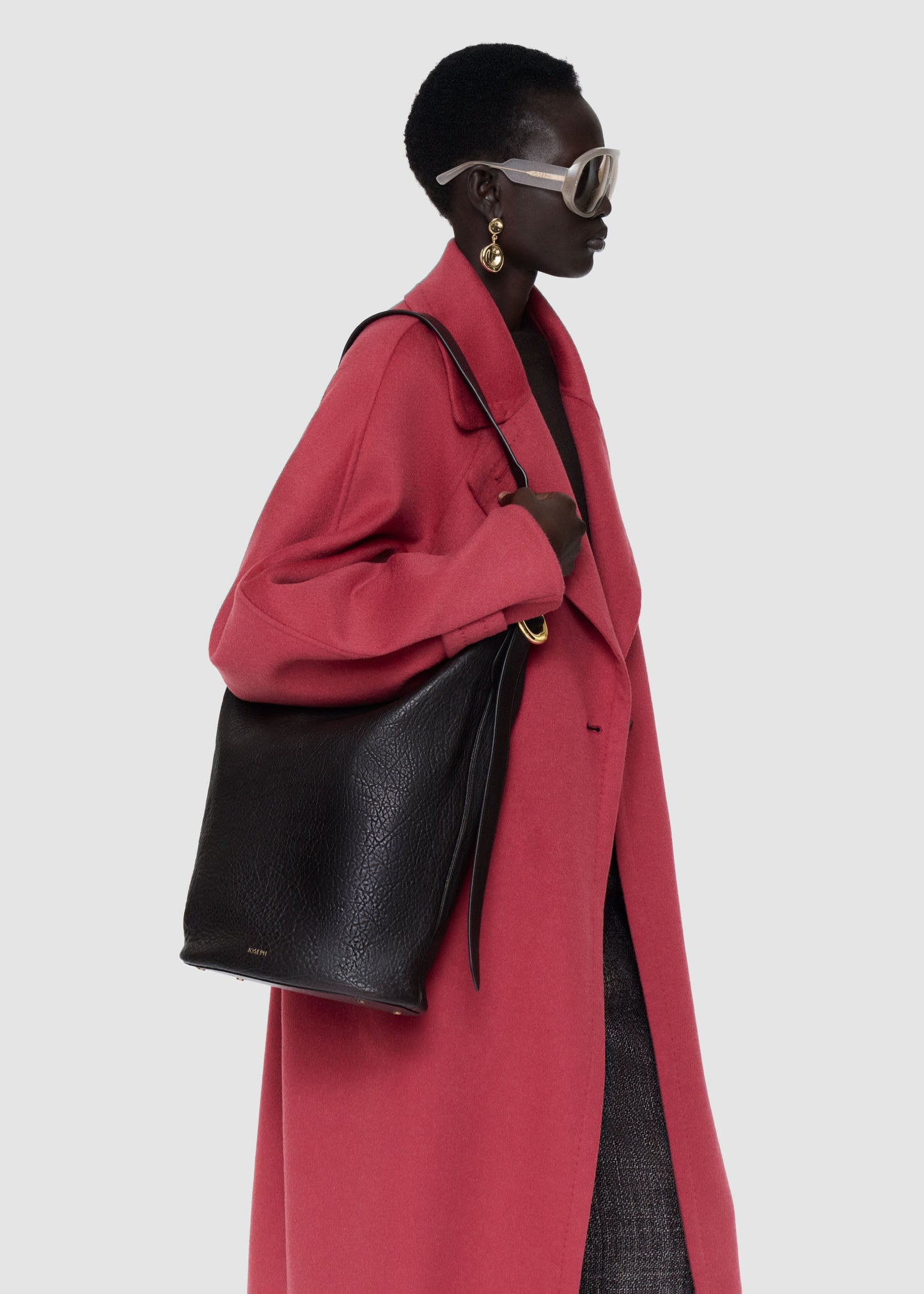Person wearing a long red coat holding a black handbag on a white background
