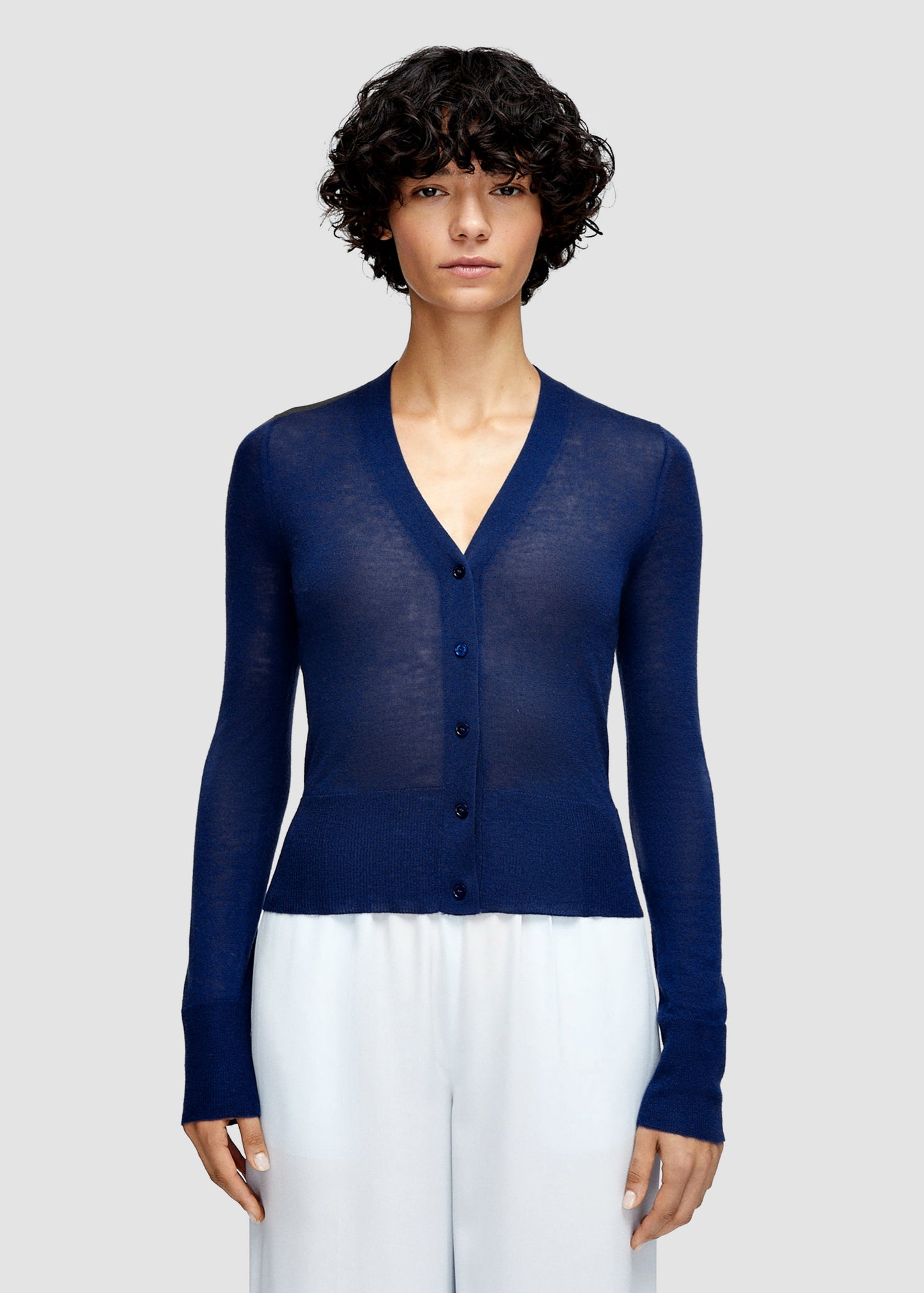 Woman wearing a blue cardigan over a white top on a light gray background