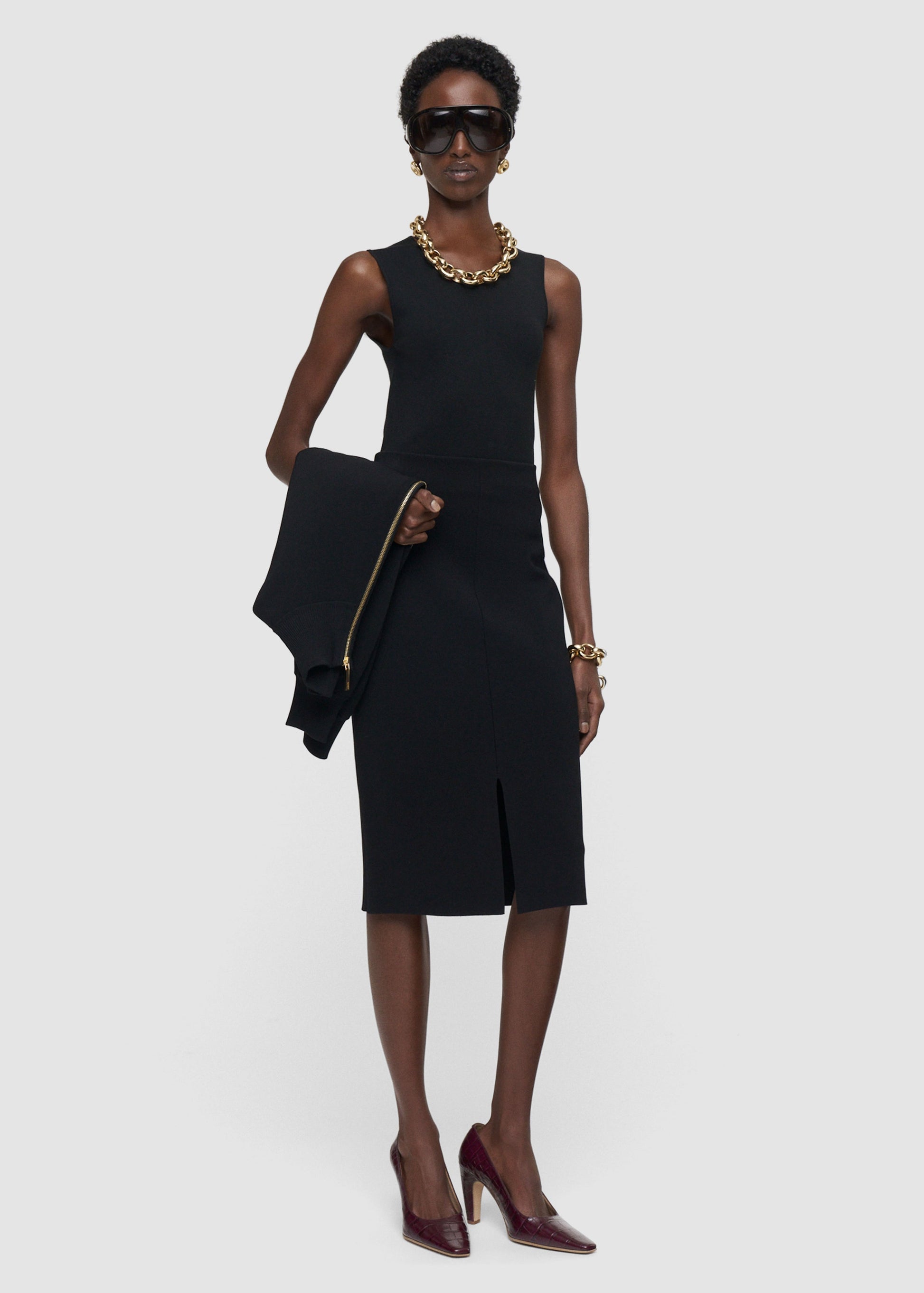 Woman wearing a black dress holding a black jacket on a white background