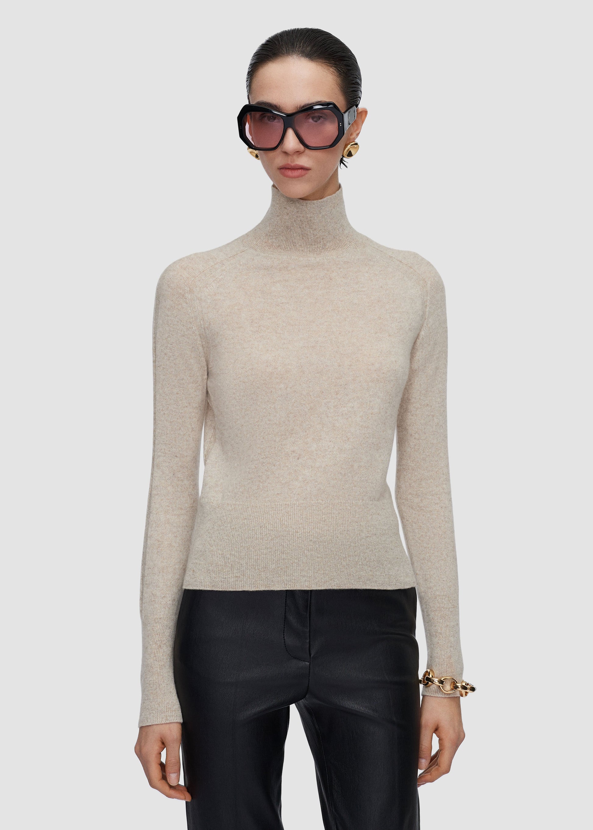 Person wearing a beige turtleneck sweater and black pants on a white background