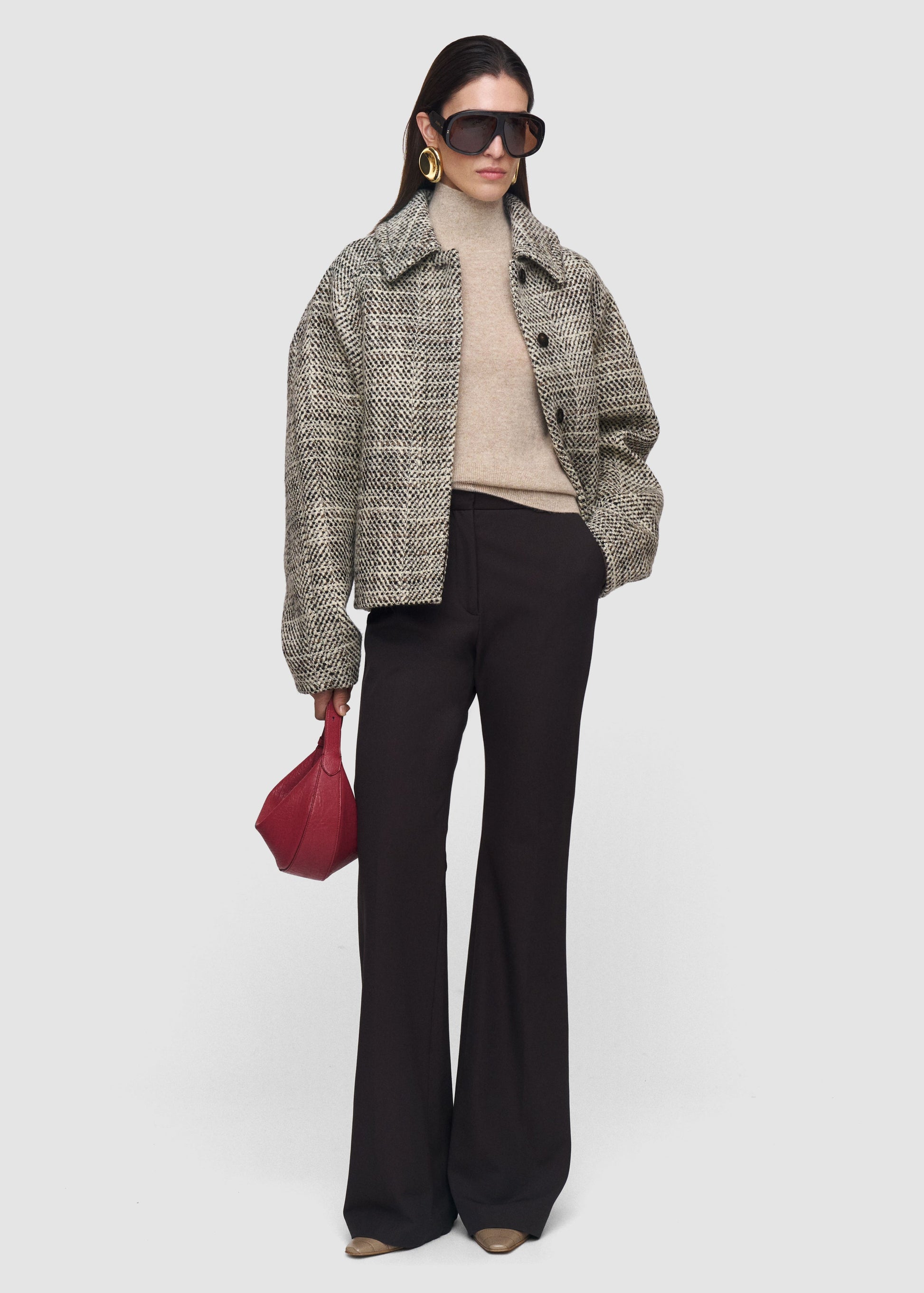 Woman wearing a checkered coat, beige sweater, black pants, and sunglasses on a white background