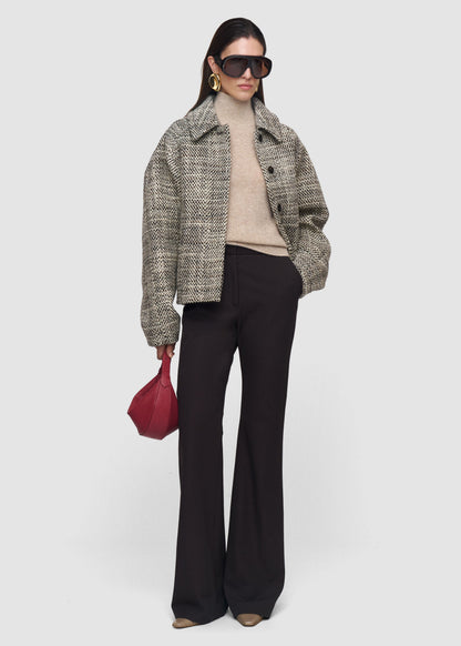 Woman wearing a checkered coat, beige sweater, black pants, and sunglasses on a white background