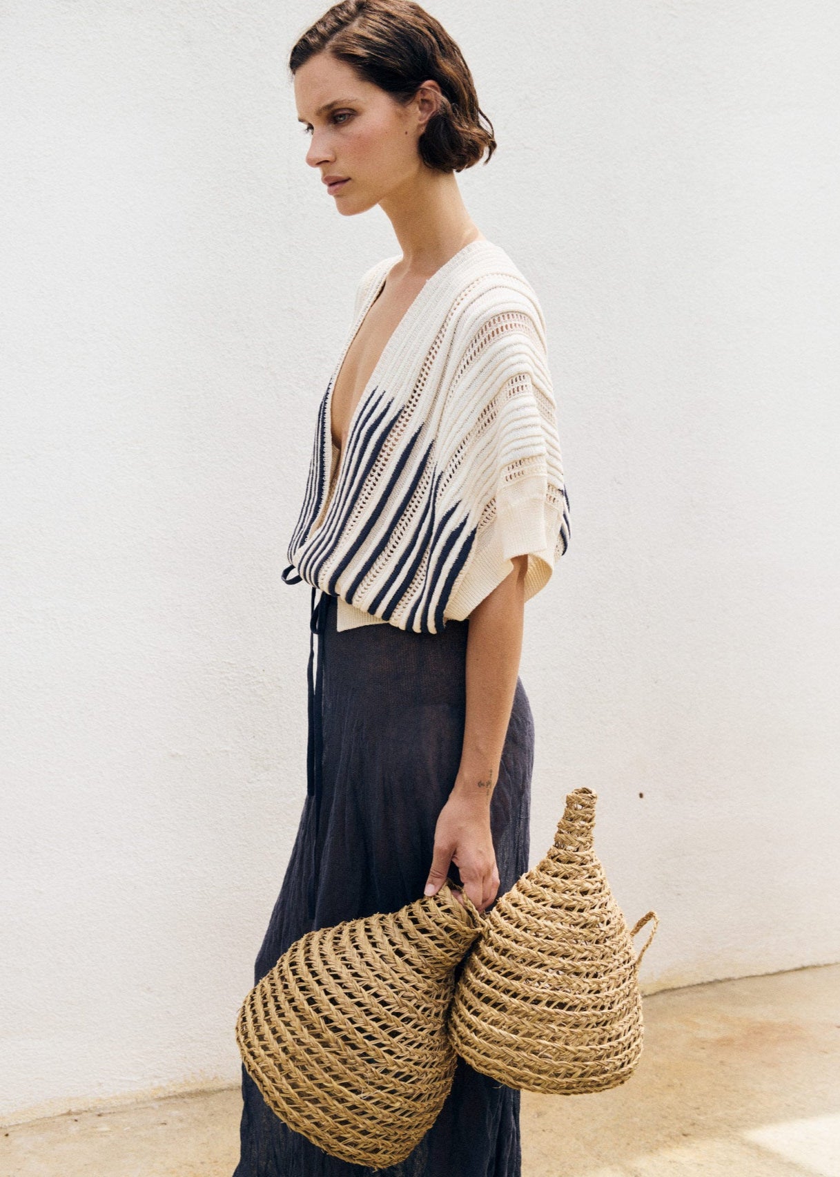 Woman holding two woven bags against a plain background